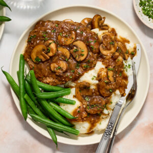 cube steak on a white plate with mashed potatoes and green beans