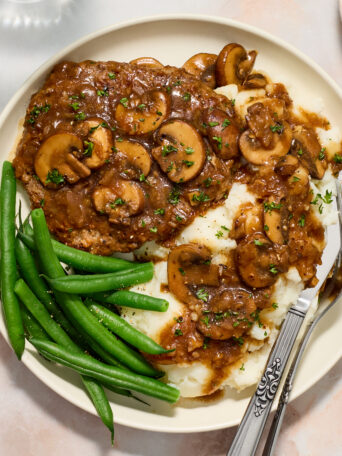 cube steak on a white plate with mashed potatoes and green beans