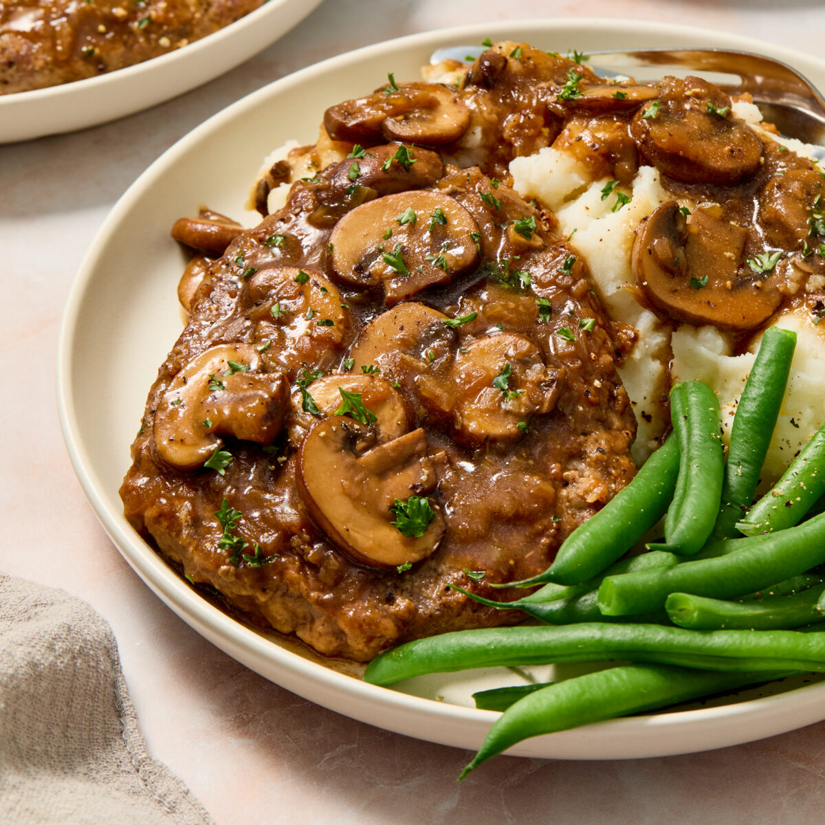 cube steak on a white plate with mashed potatoes and green beans