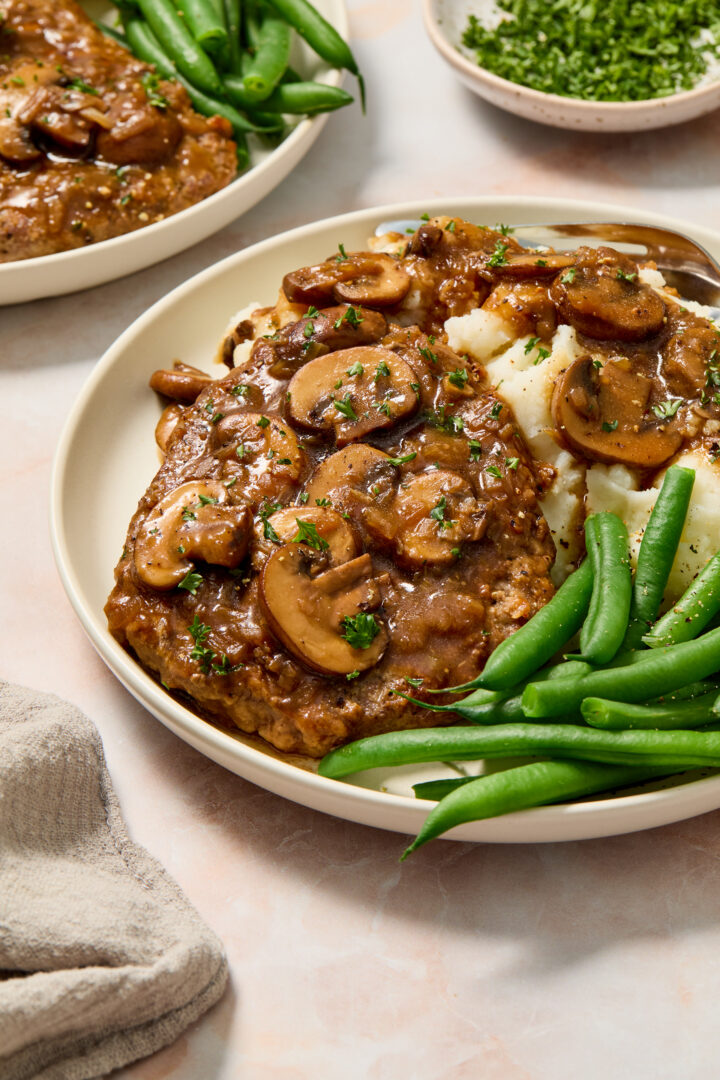 cube steak on a white plate with mashed potatoes and green beans