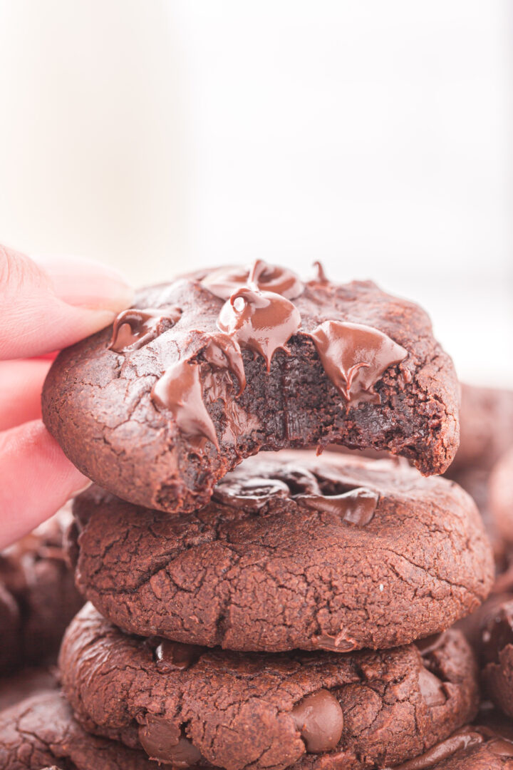 a stack of cookies with a hand shown holding one cookie with a bite taken out of it