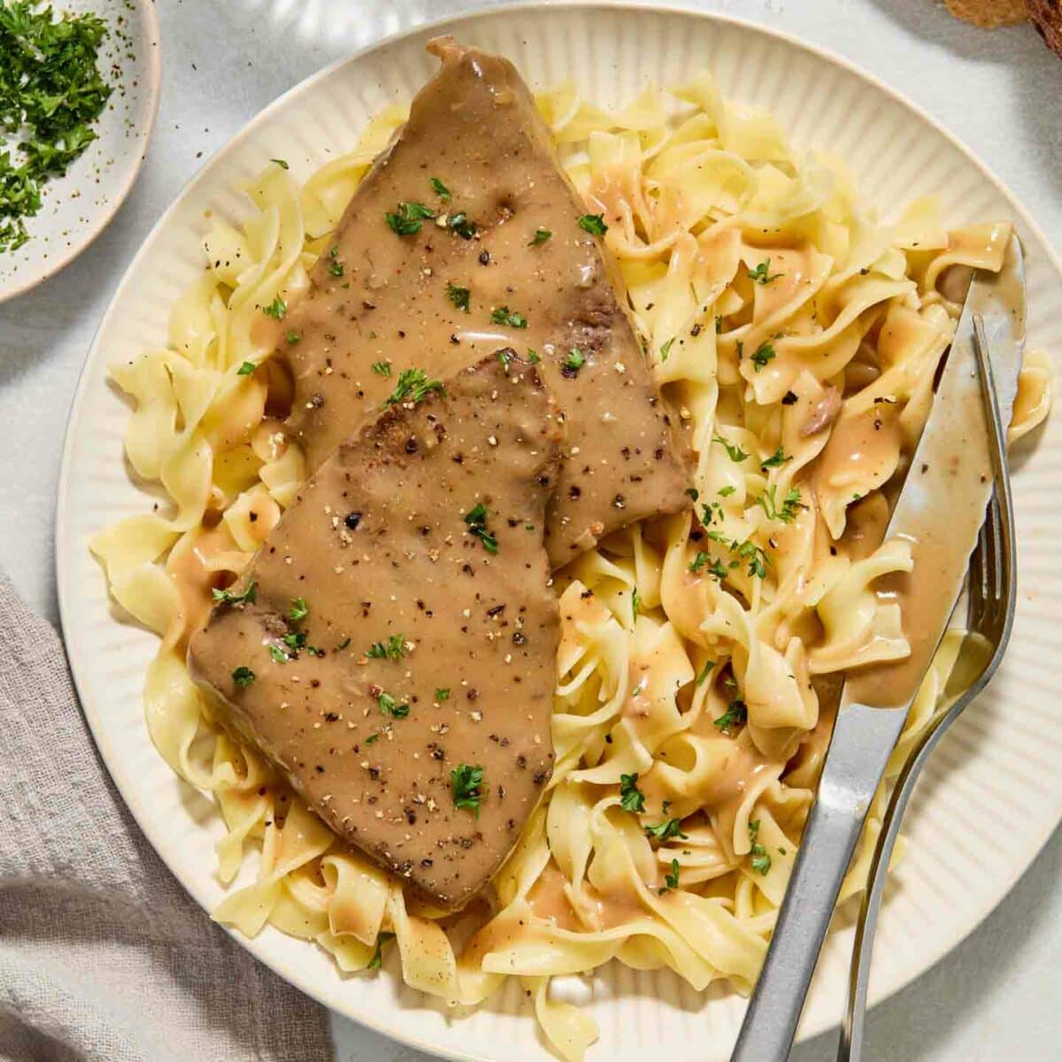 round steak with gravy on top of noodles on a white plate