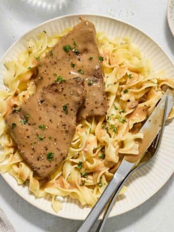 round steak with gravy on top of noodles on a white plate