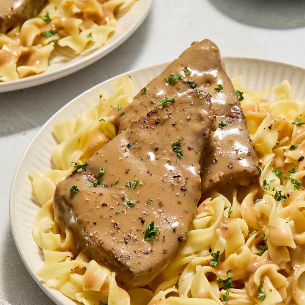 round steak with gravy on top of noodles on a white plate