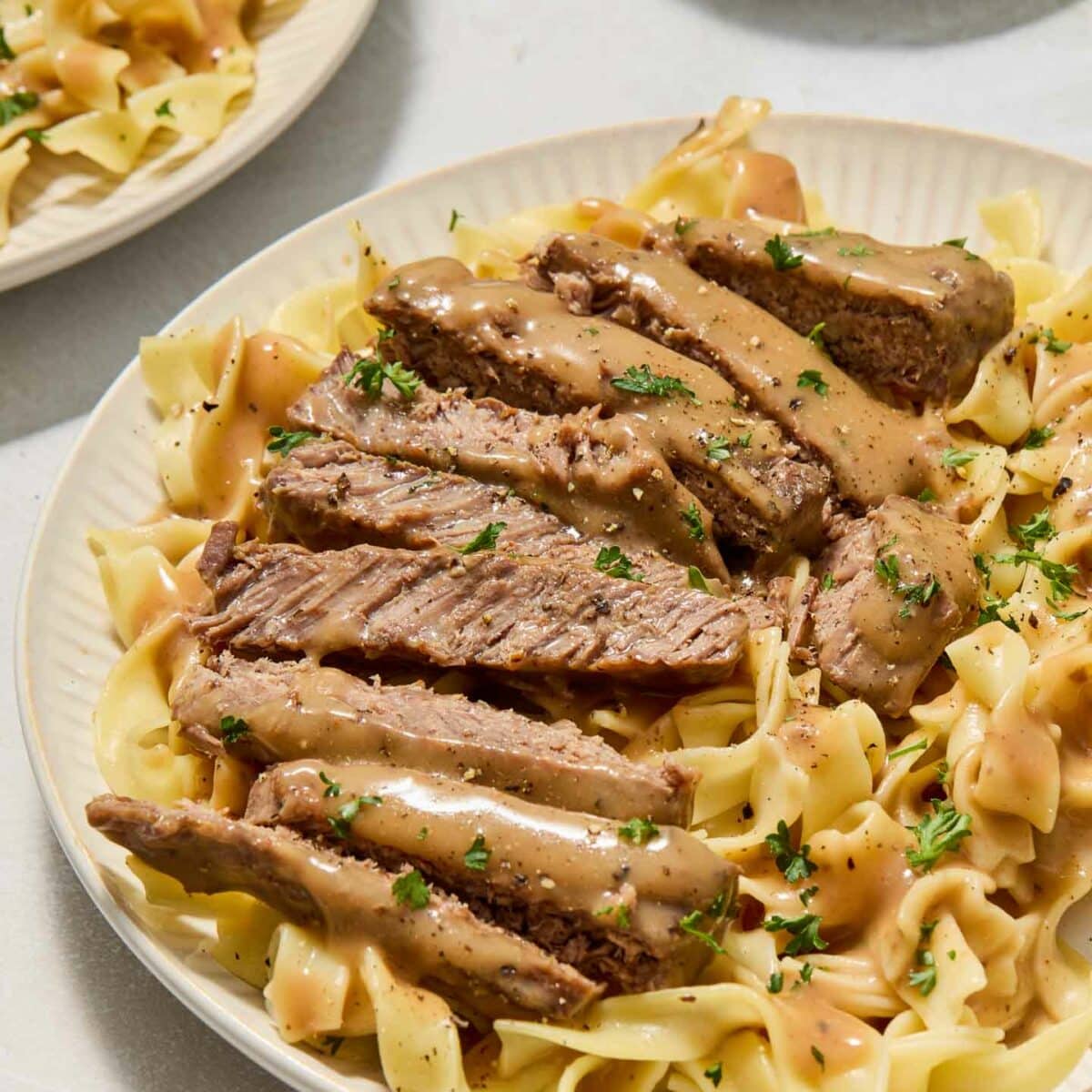 round steak with gravy on top of noodles on a white plate