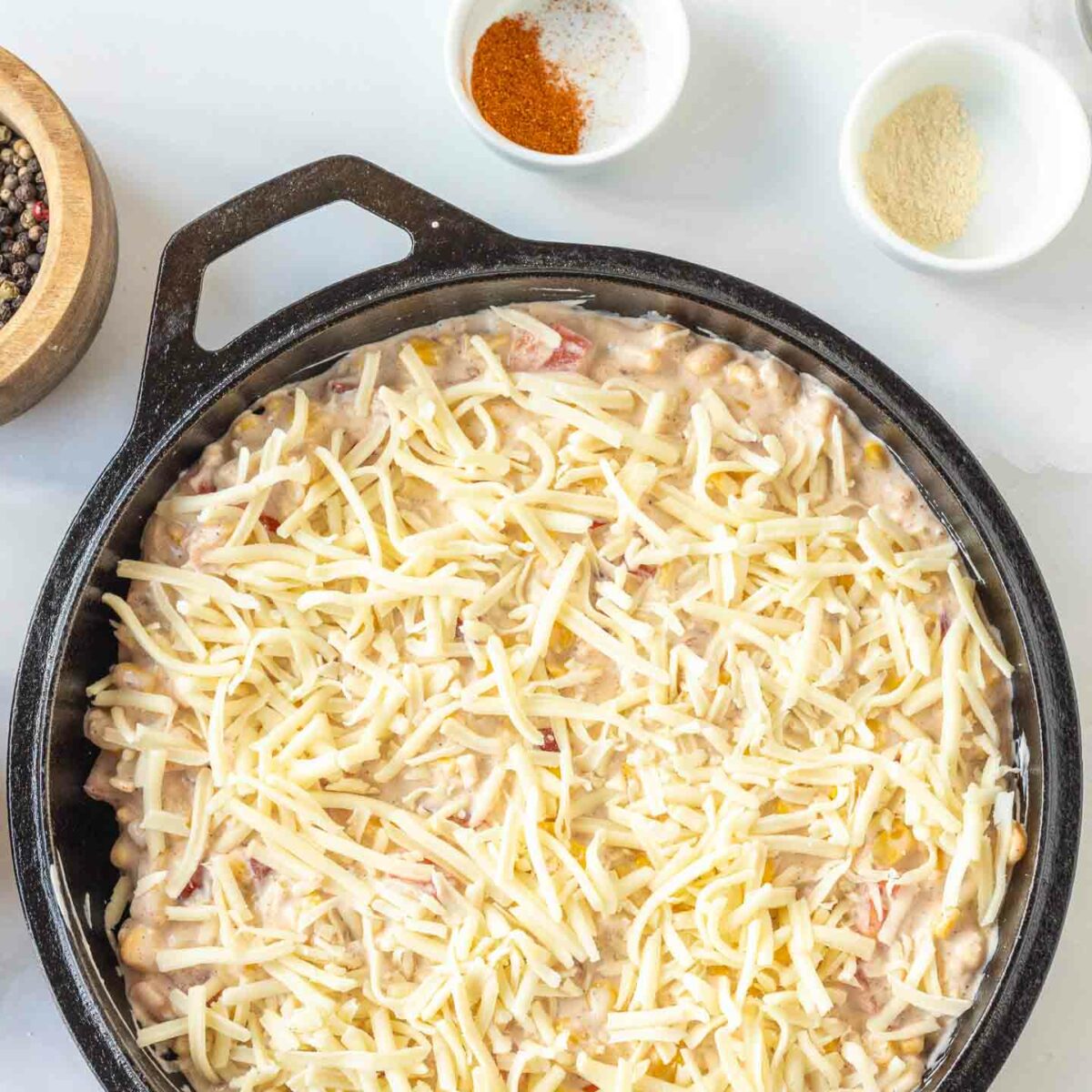 corn dip in a black skillet with shredded cheese on top