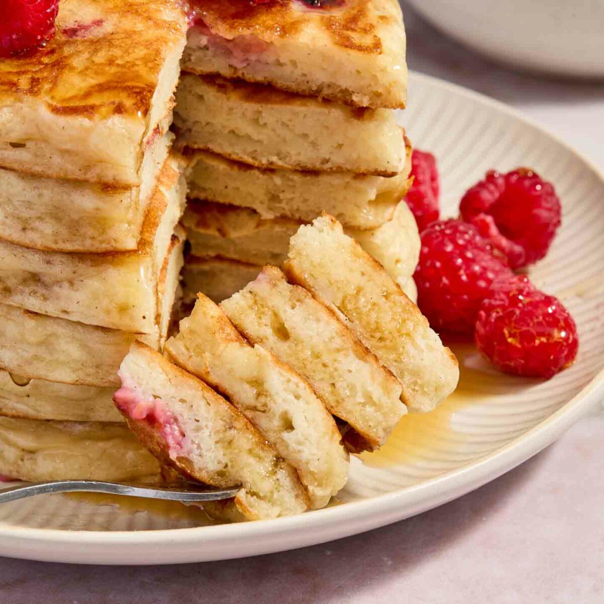 a forkful of pancakes shown on a white plate with a stack of pancakes
