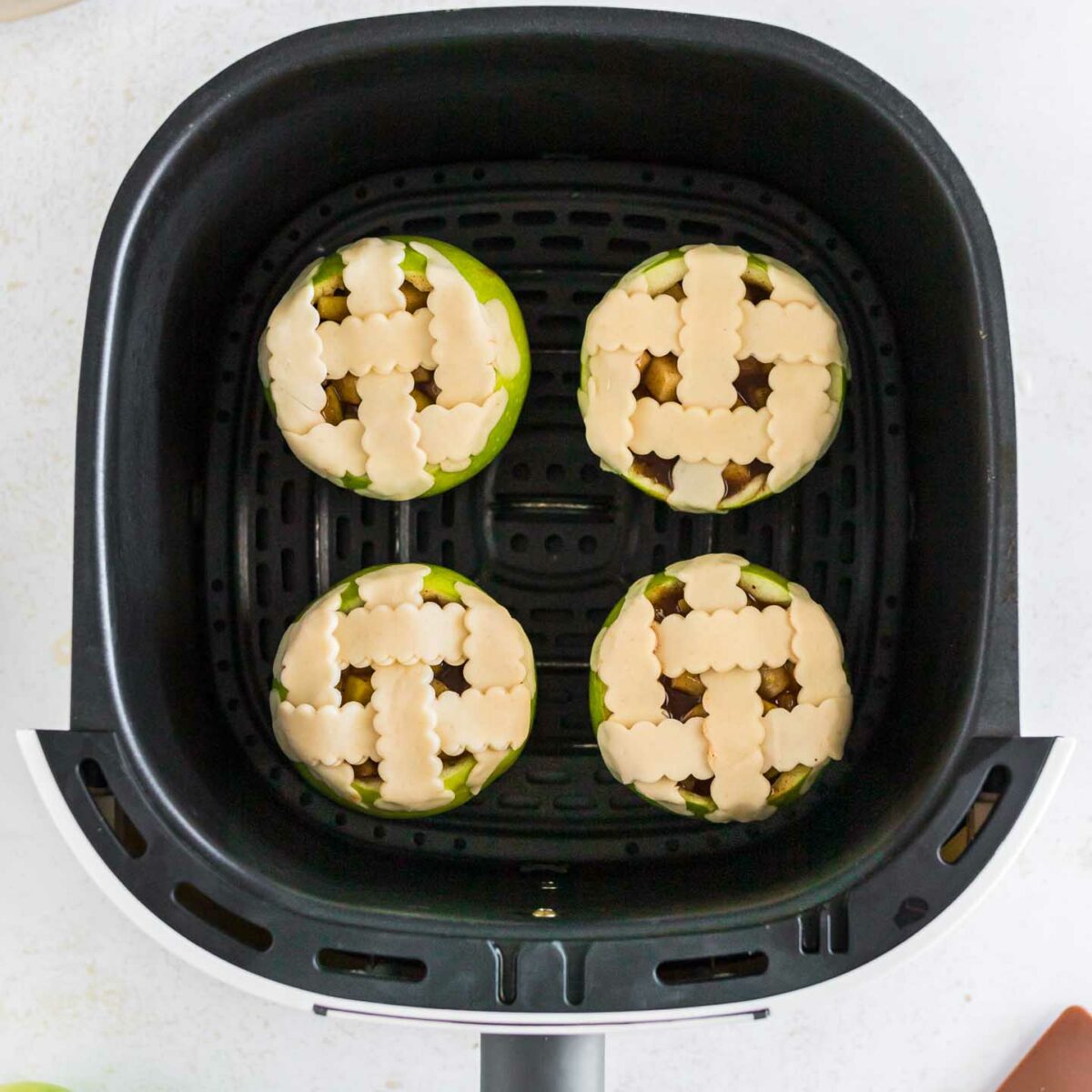 four apples with a lattice pie crust on top in the air fryer basket