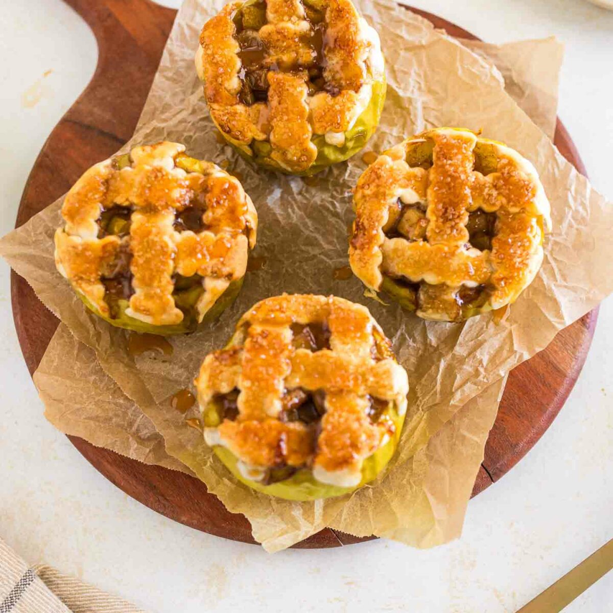 four baked apples with lattice pie crust on top on a wooden board