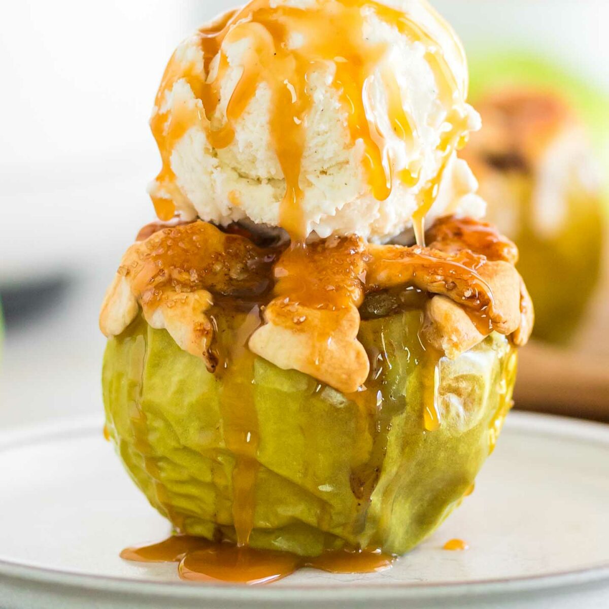 baked apple on a white plate with a scoop of vanilla ice cream and caramel drizzle