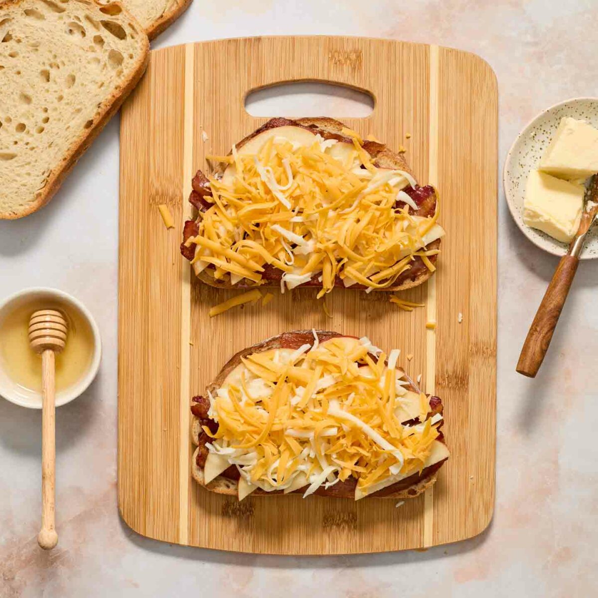 bread slices with bacon, honey, apples and cheese on a cutting board