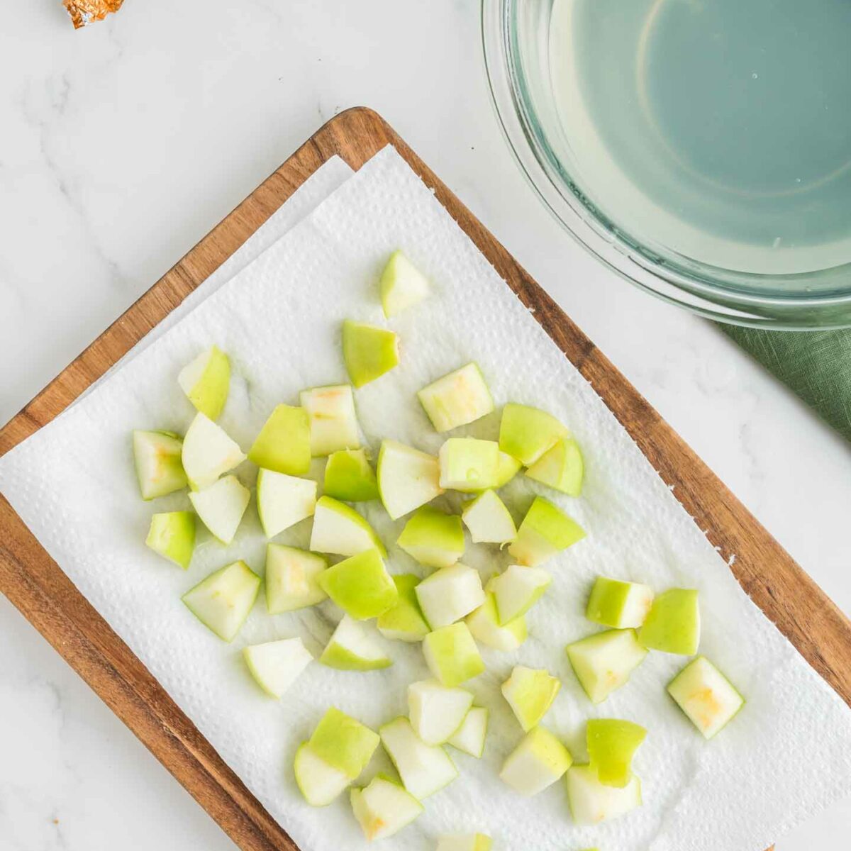 apple slices cut into cubes on a brown cutting board with parchment paper