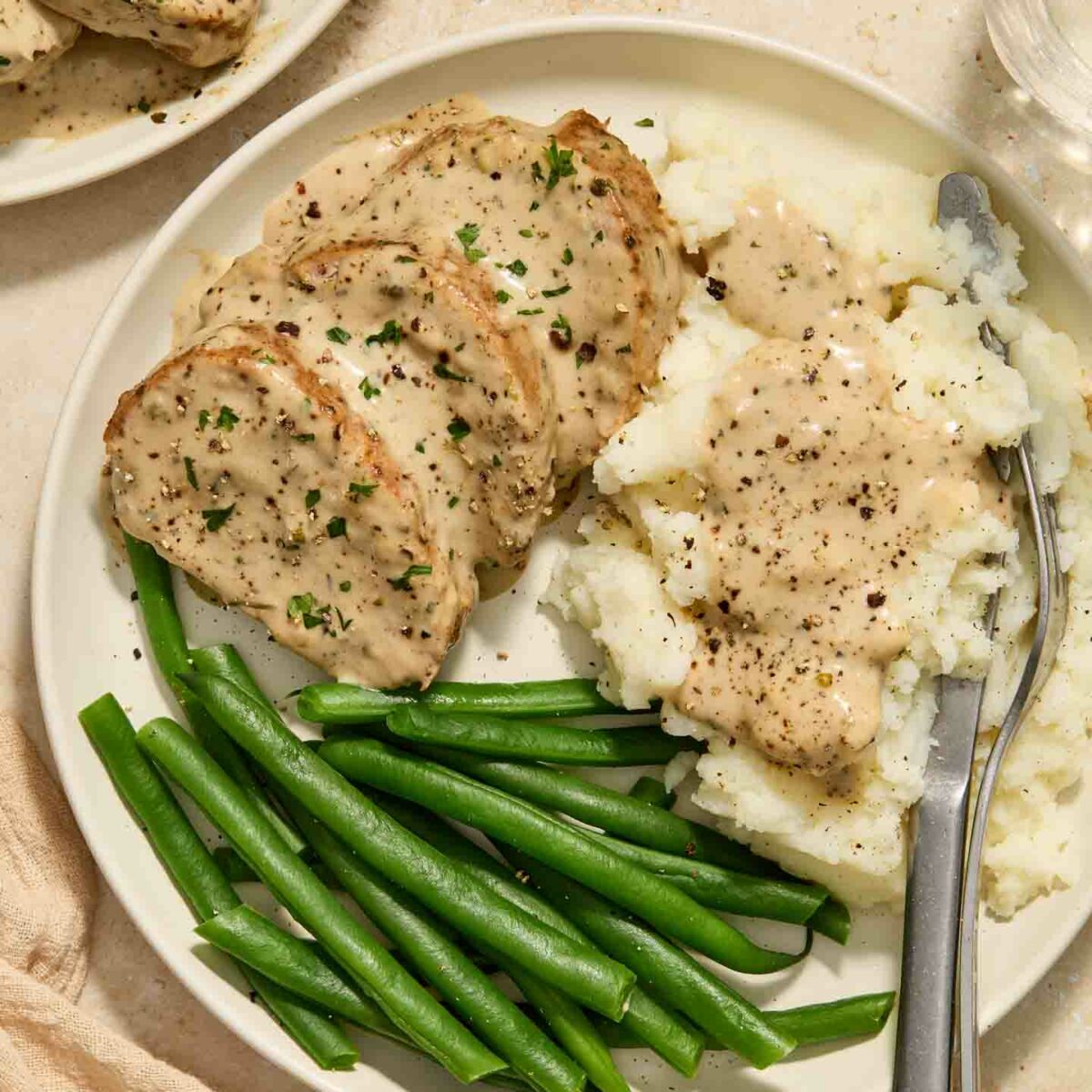 pork tenderloin with cream sauce on a white plate with mashed potatoes and green beans