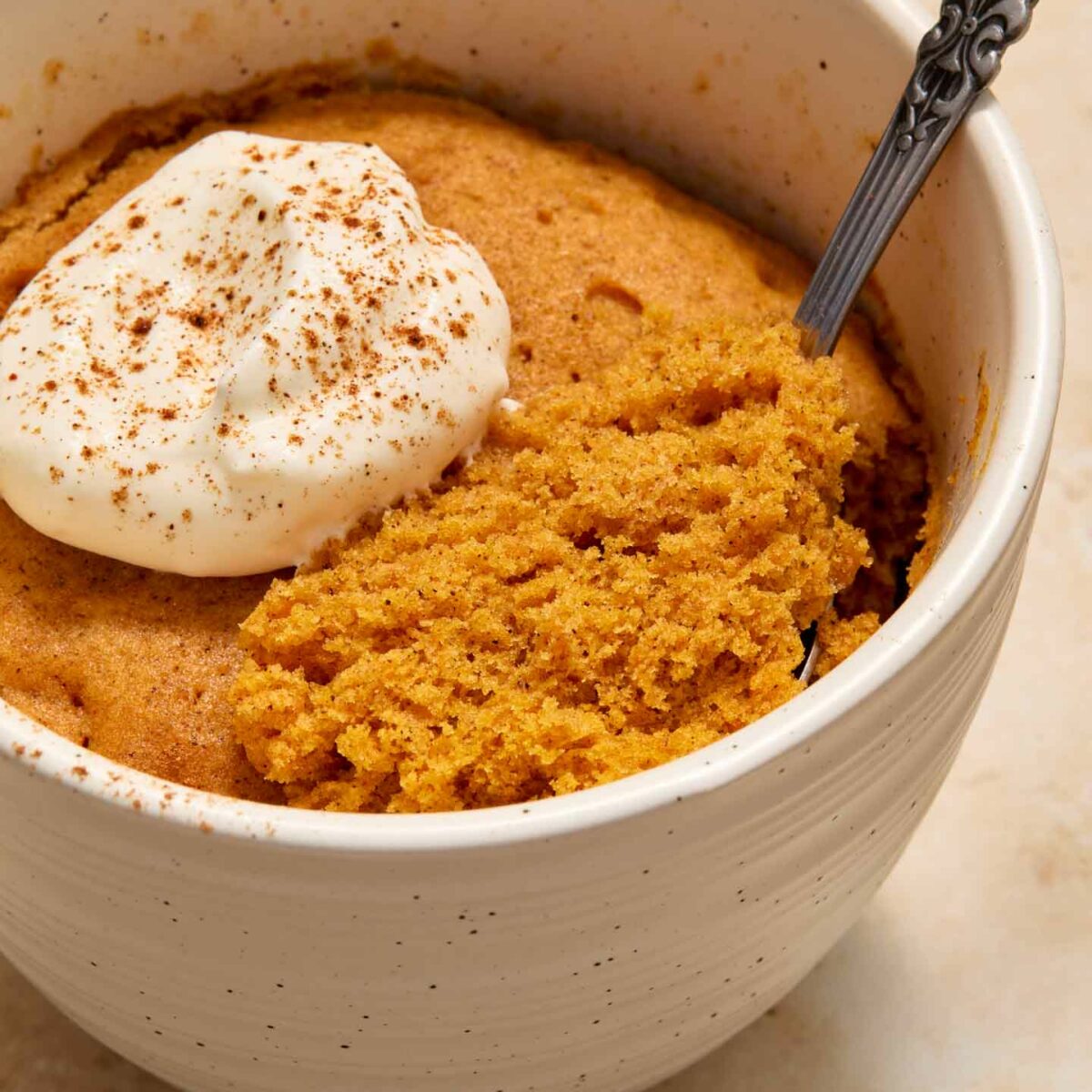 cake in a white mug with whipped cream and a spoonful of cake shown