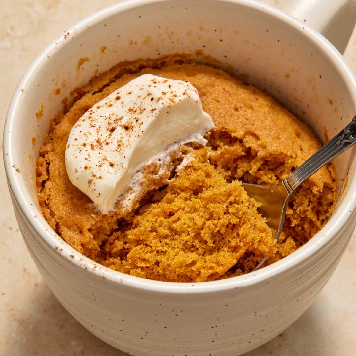 cake in a white mug with whipped cream and a spoonful of cake