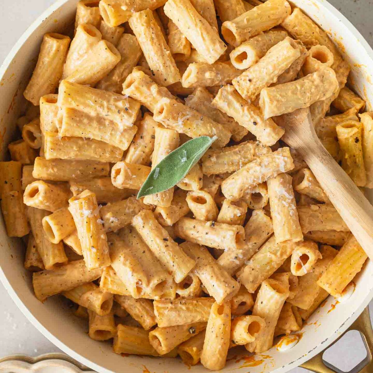 pumpkin alfredo pasta in a white skillet with a sprig of sage