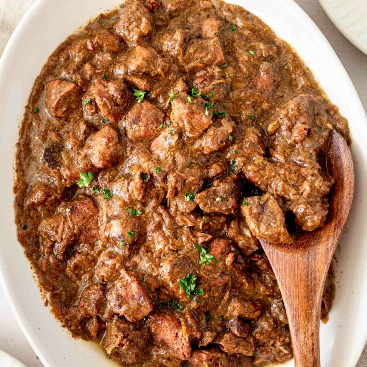 steak bites in a white serving dish showing a few pieces of steak bites on a wooden spoon