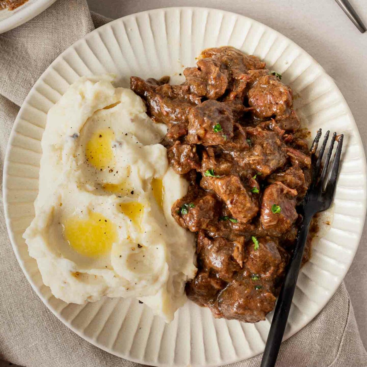 steak bites and mashed potatoes with butter on a white plate with a black fork