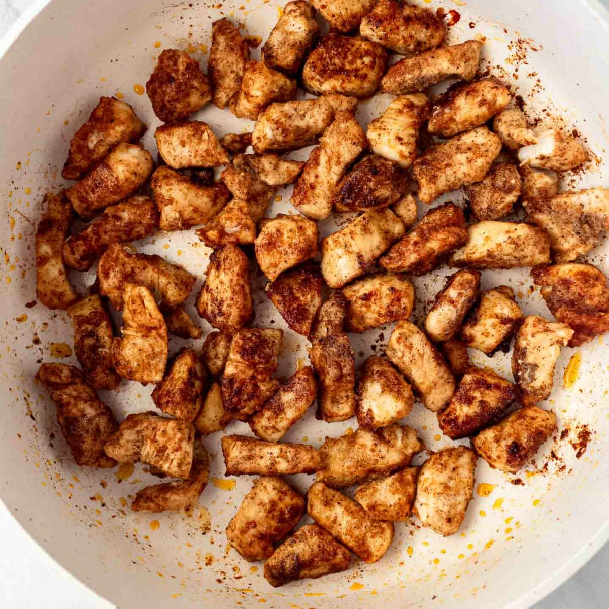 chicken cut into bite-sized pieces being cooked in a white skillet