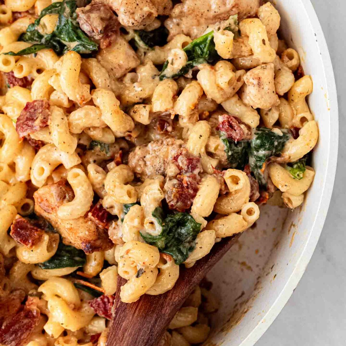 chicken mac and cheese in a white serving bowl with a wooden spoon