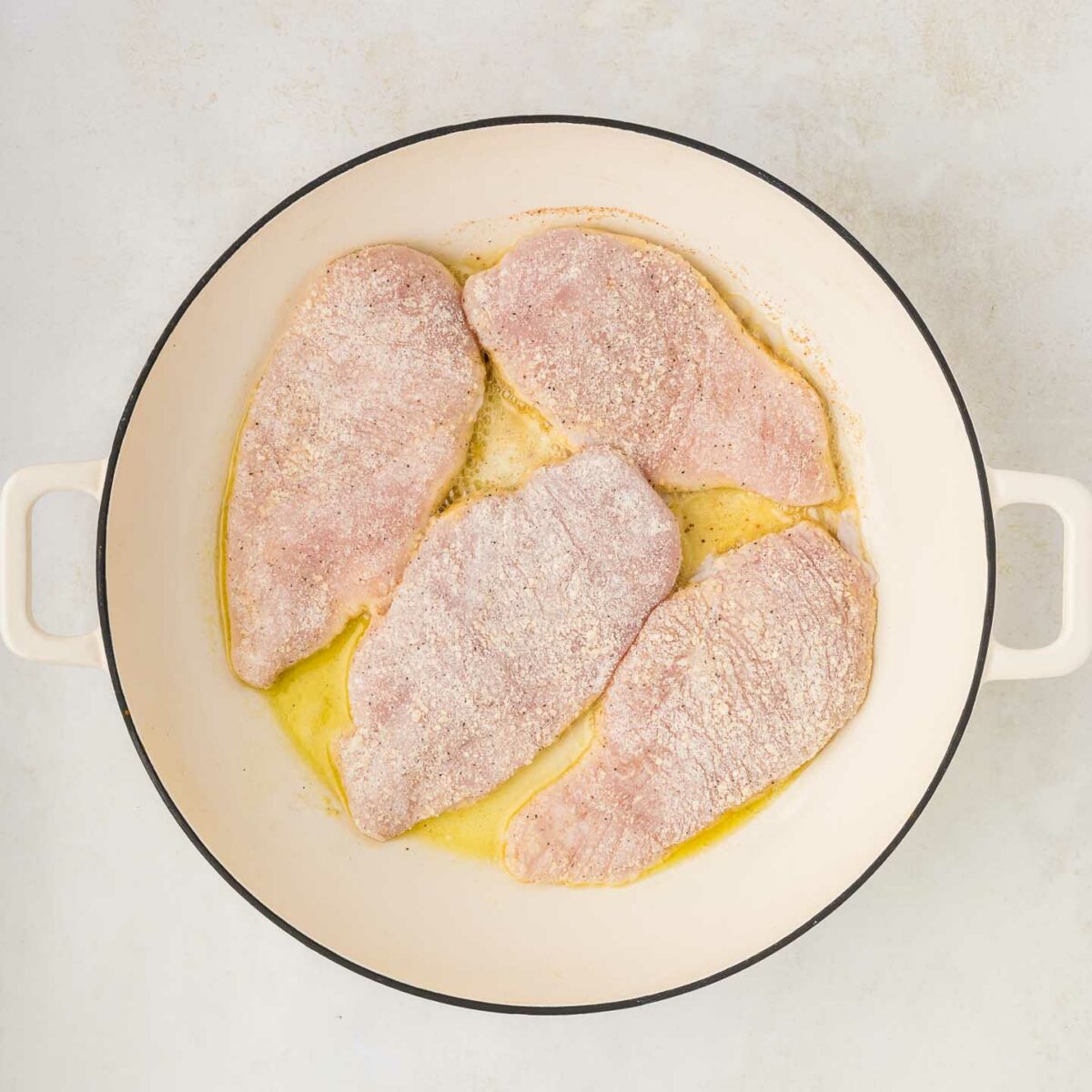 dredged chicken in a skillet with olive oil
