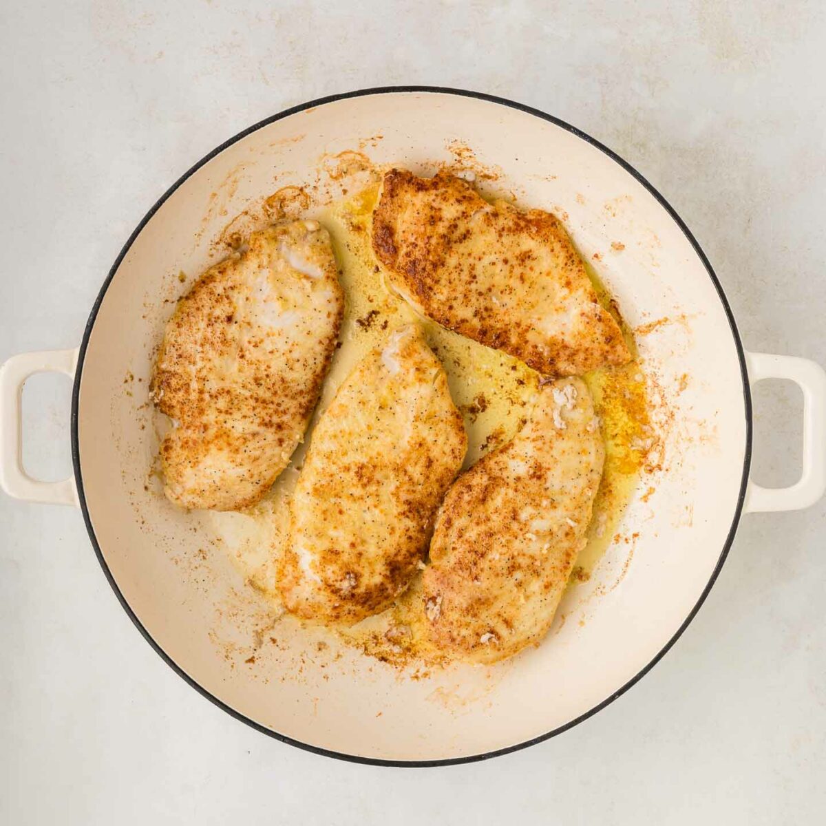 chicken seared and golden brown in a white skillet