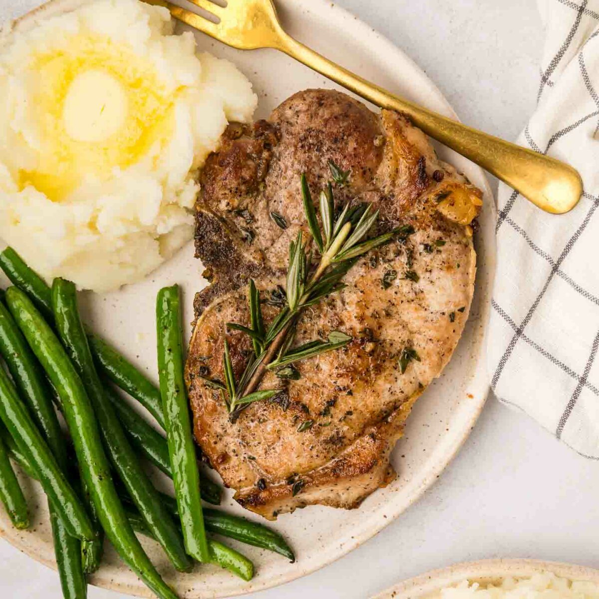 pork chops on a white plate with mashed potatoes and green beans