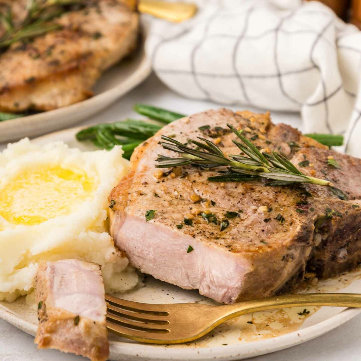 pork chops on a white plate with mashed potatoes and green beans with a bite of pork shown on a fork