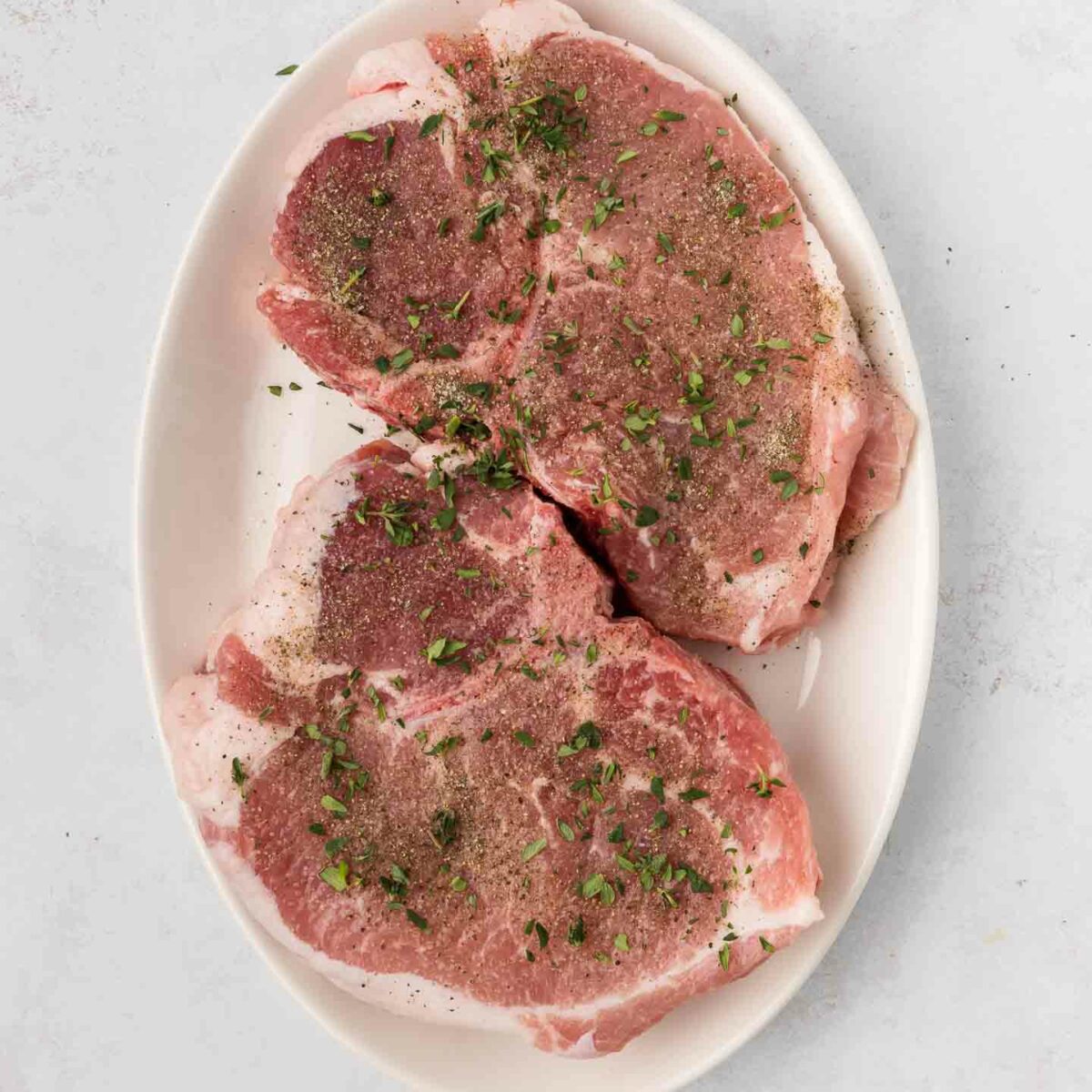 uncooked pork chops seasoned on a white plate