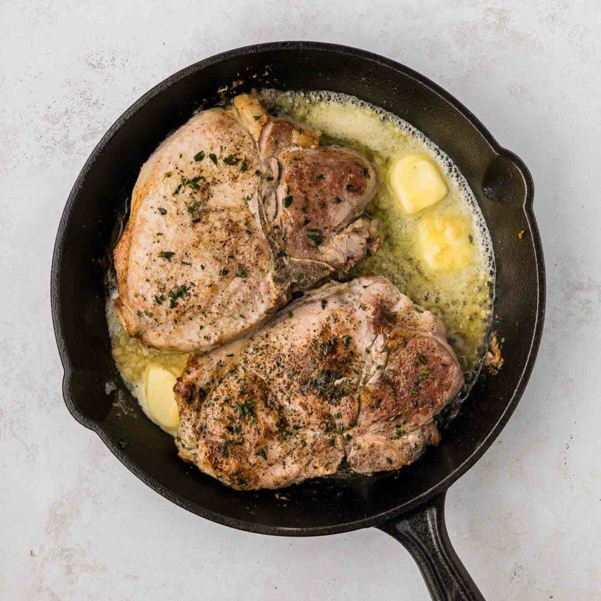 pork chops cooking in a black cast iron skillet with melted butter