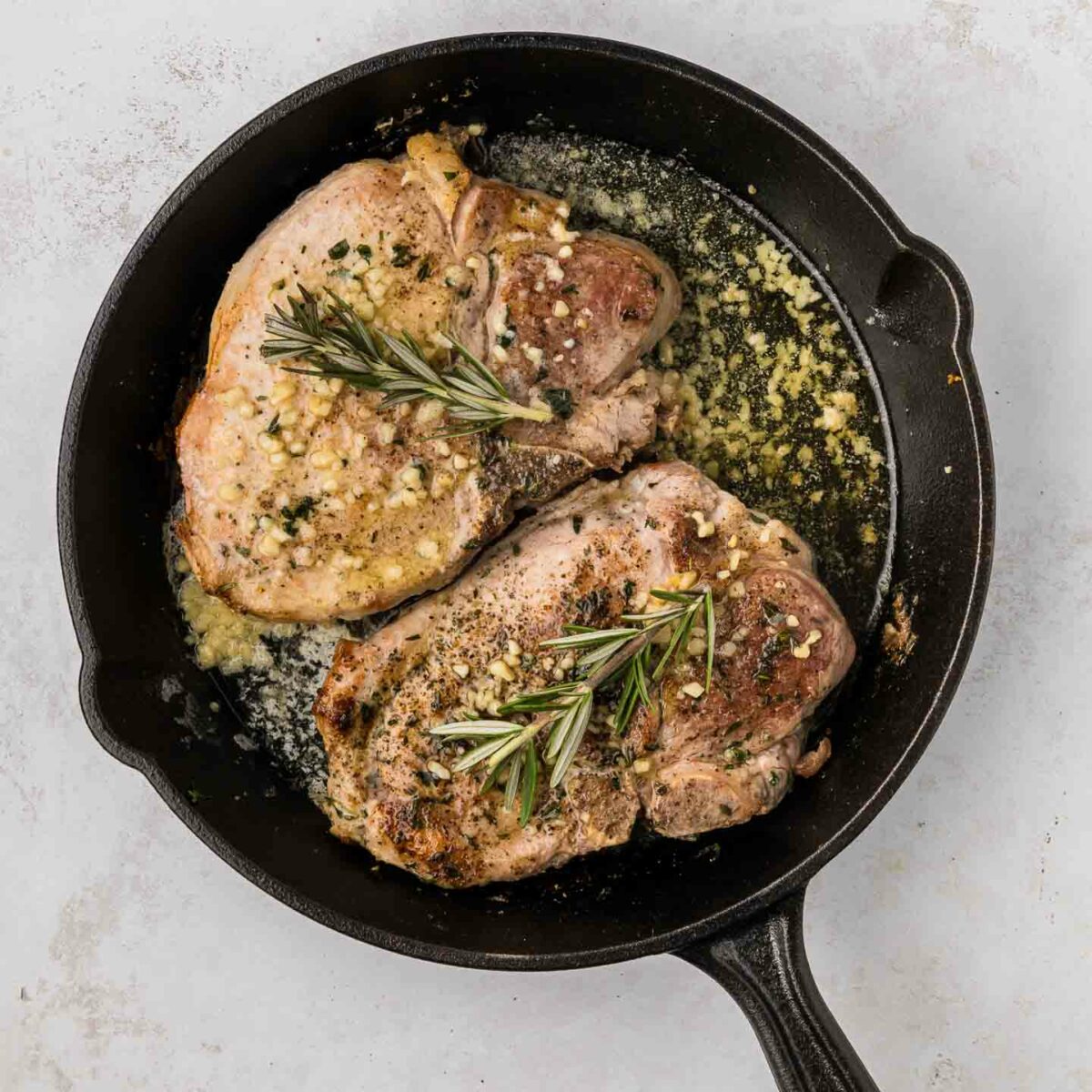 pork chops in black cast iron skillet with herbs and rosemary on top of pork