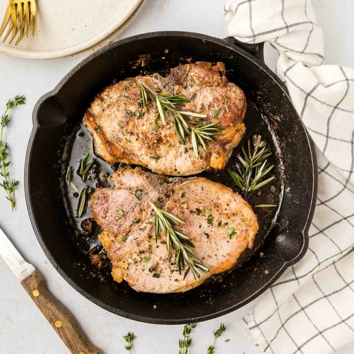 pork chops in a black cast iron skillet with rosemary and herbs