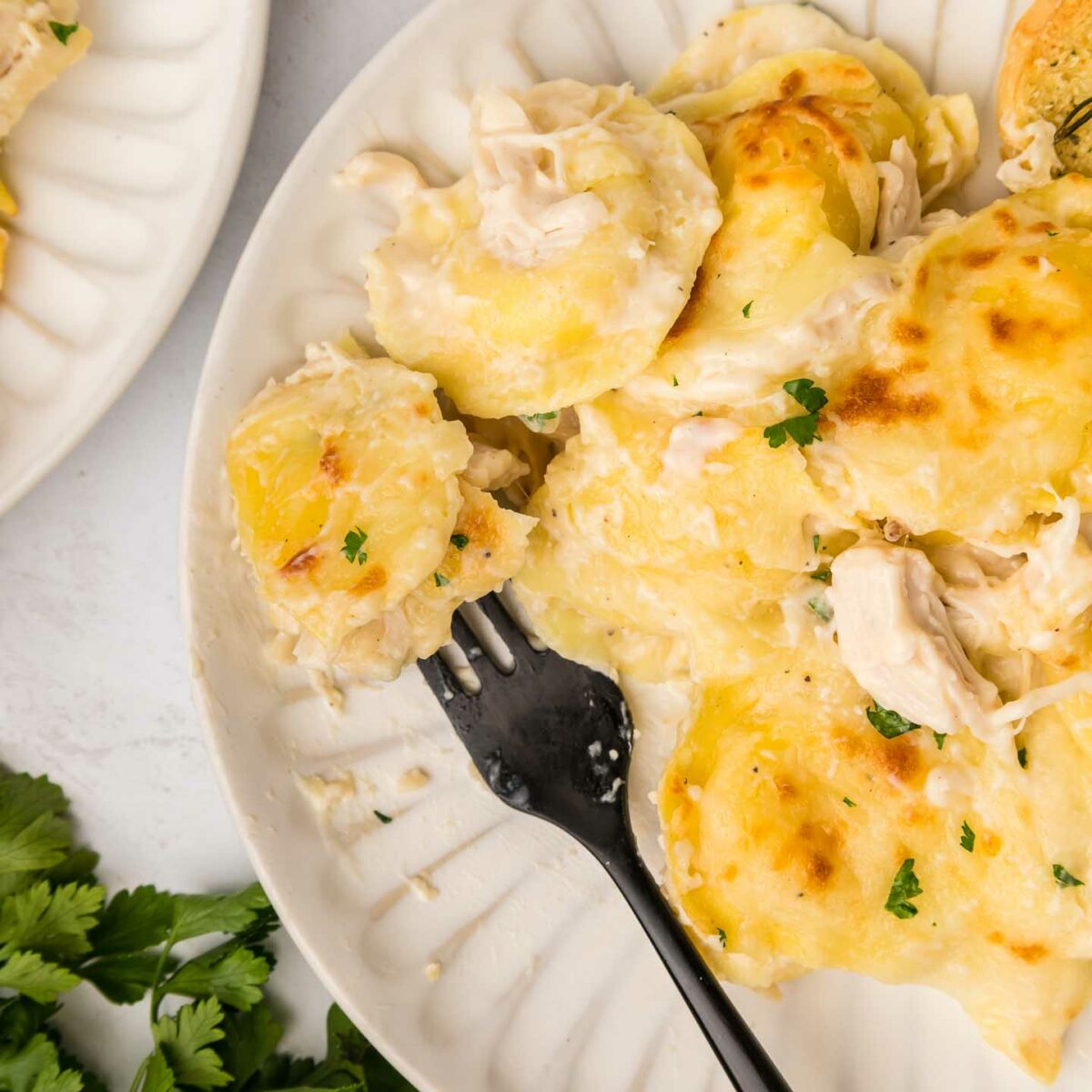 baked ravioli on a white plate with a black fork