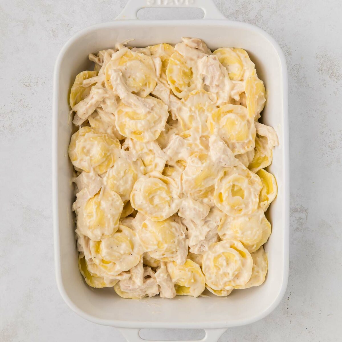 ravioli and chicken layered in a white dish