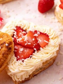 heart puff pastry with white chocolate mousse and sliced strawberries on a light pink surface