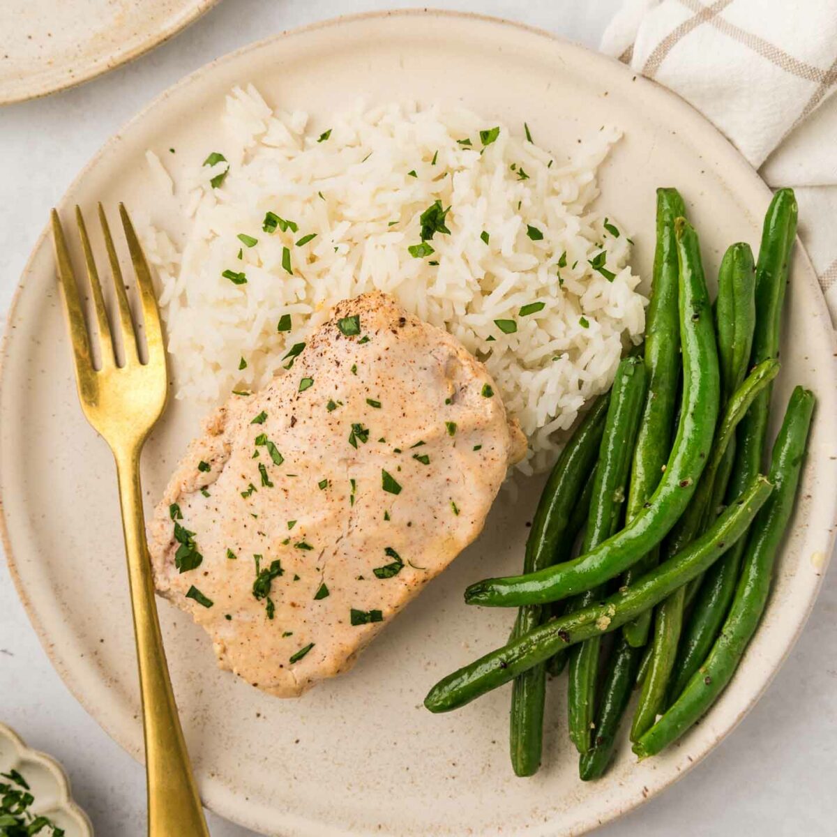 overhead photo of pork chop on a plate with a fork, mashed potatoes, and green beans