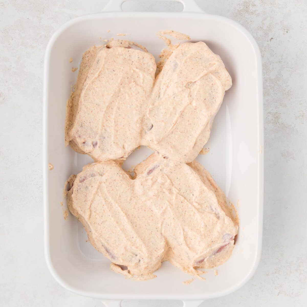 four pork chops in a white baking dish covered with Greek yogurt mixture