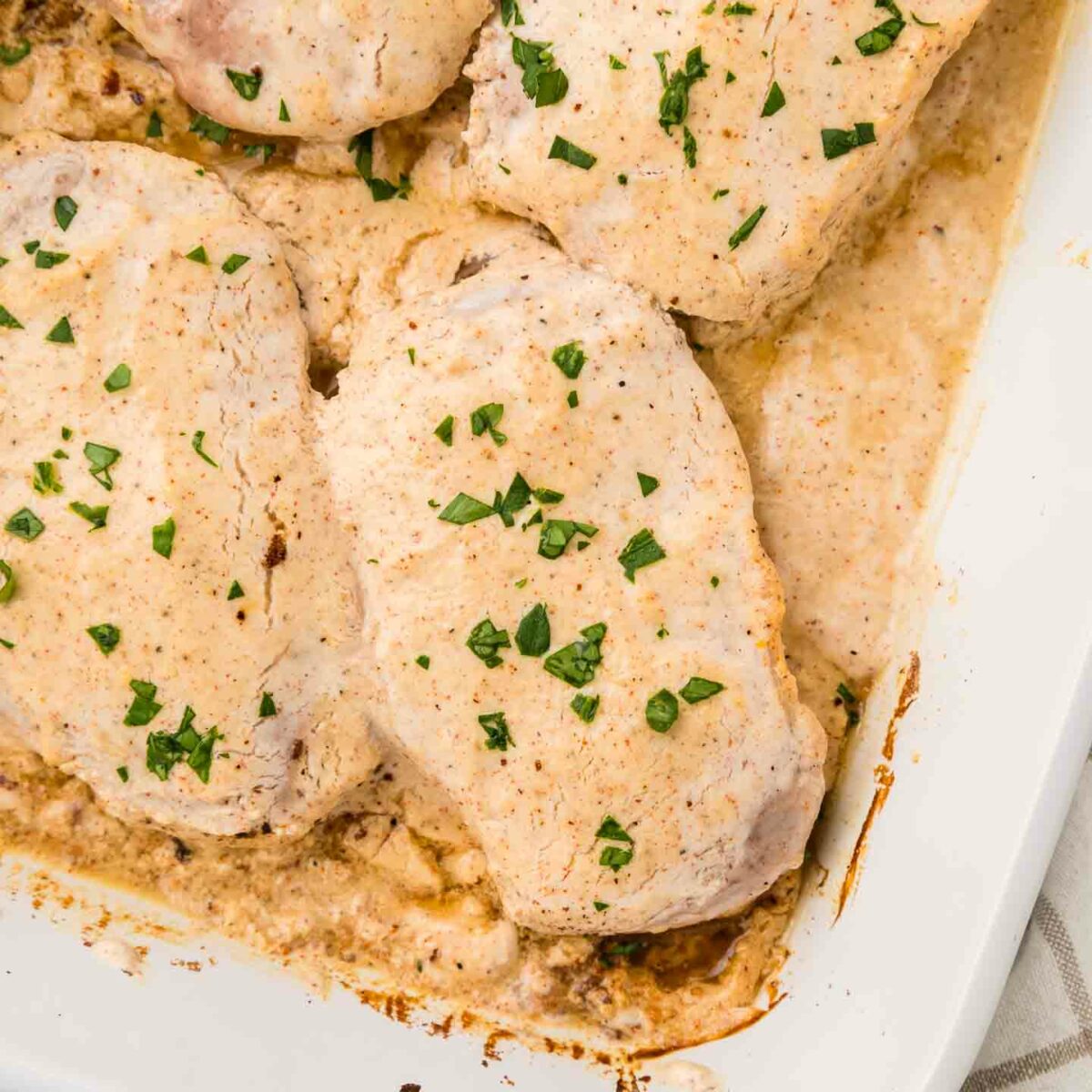 four pork chops shown in a white baking dish