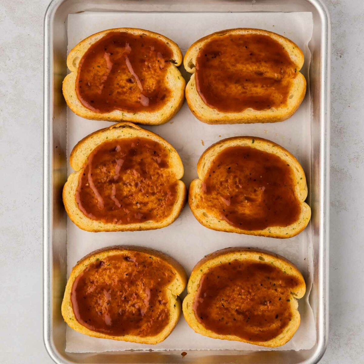 bbq sauce spread on top of toast on a sheet pan