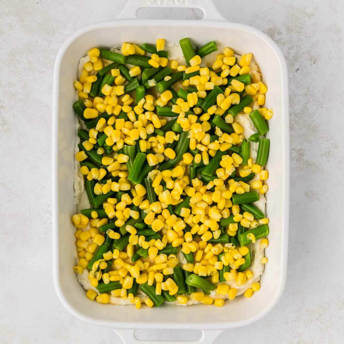 green beans and corn layered on top of mashed potatoes in a white dish