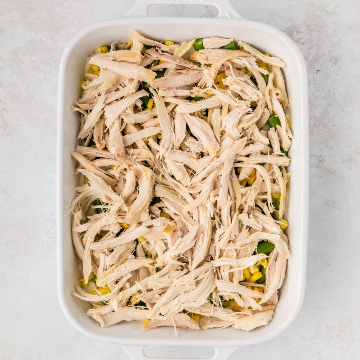 chicken layered on top of green beans and corn in a white dish