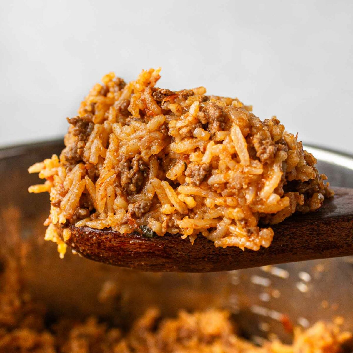taco rice on a wooden spoon shown above the pressure cooker