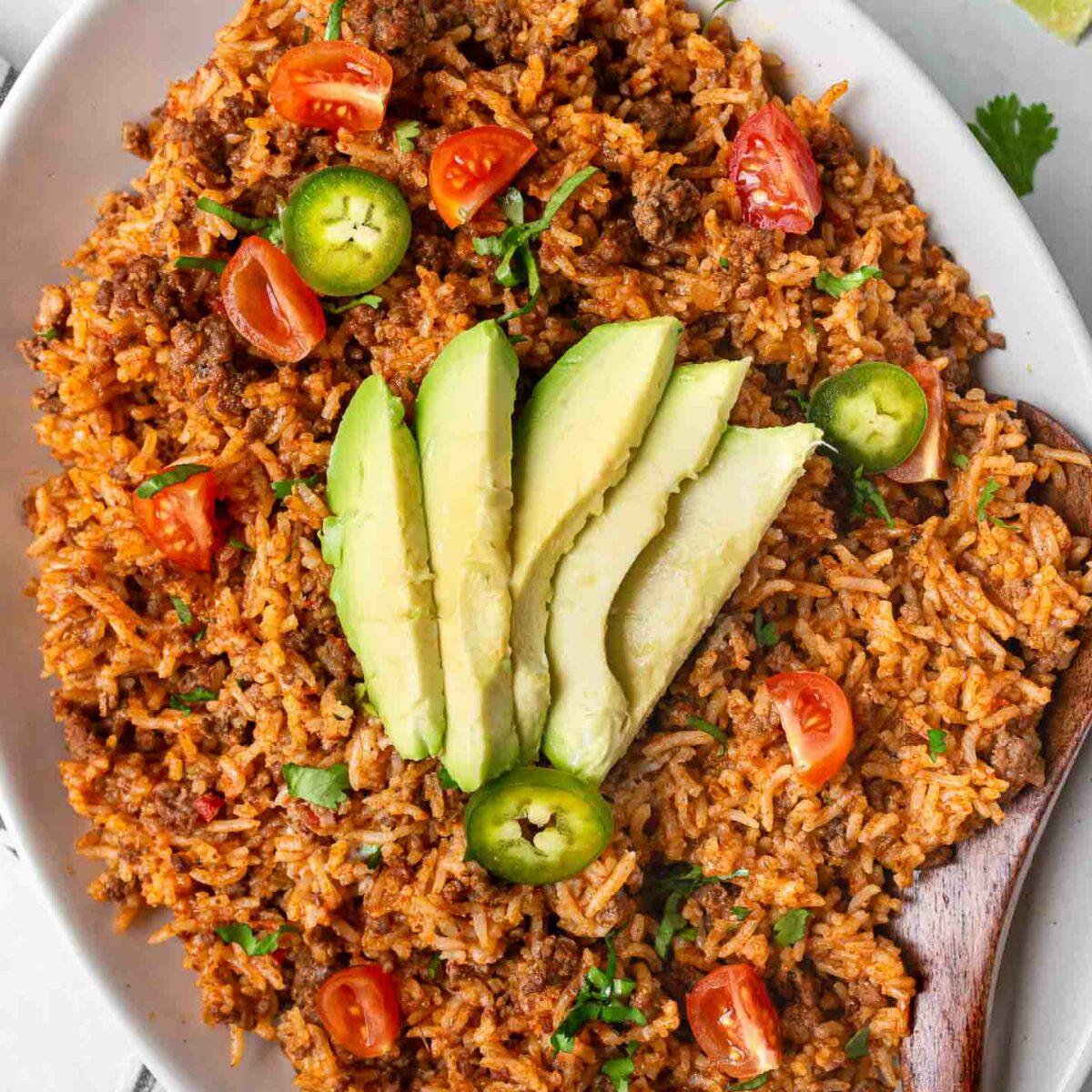 taco rice on a white platter with avocado slices and diced jalapeños
