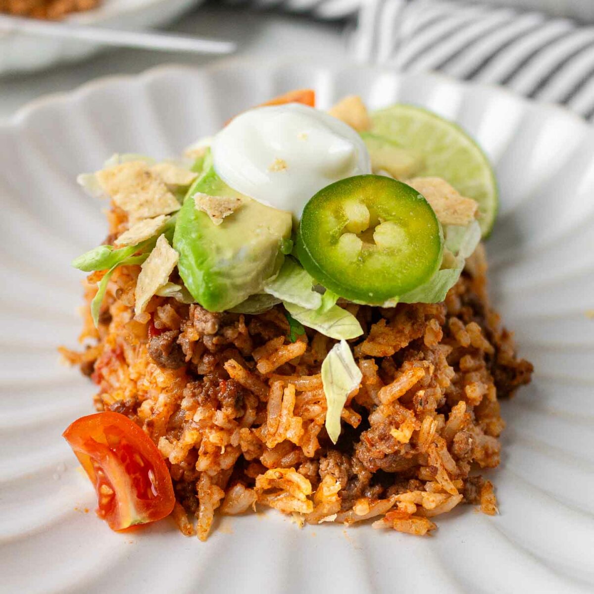taco rice shown on a white plate with sliced avocado, jalapeno, and sour cream