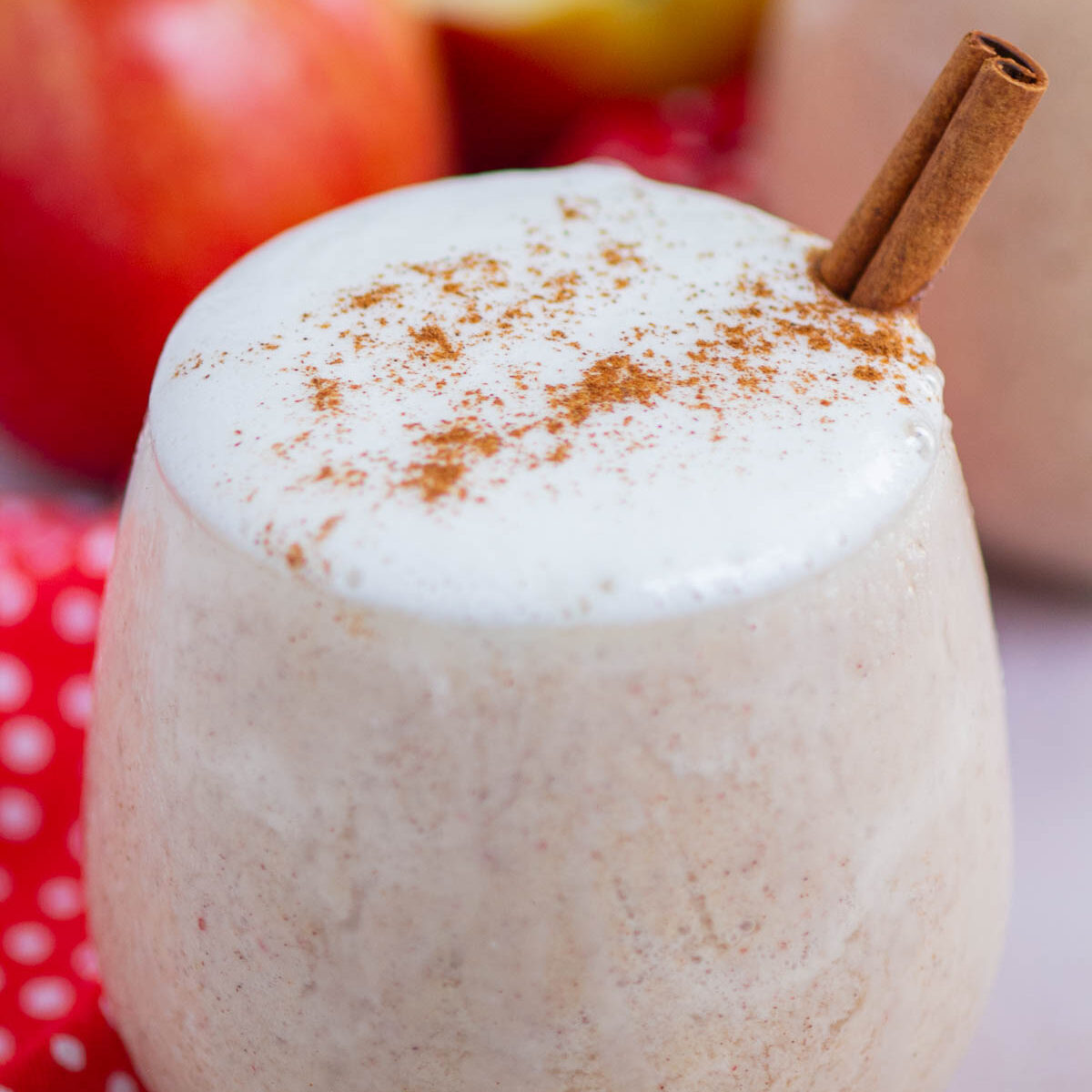 smoothie in a clear glass with a cinnamon stick and cinnamon sprinkled on top