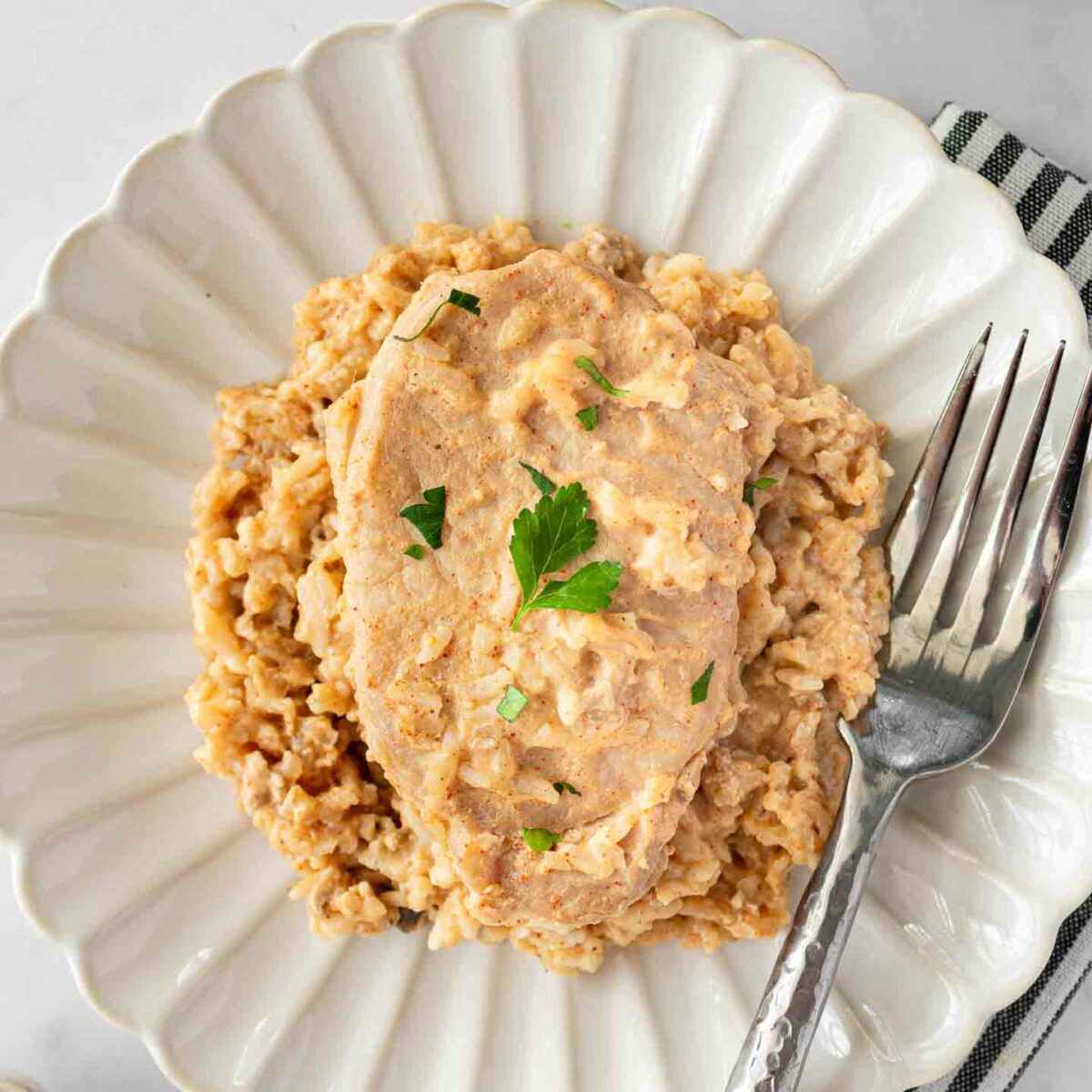 pork chops and rice on a white plate with a silver fork resting on plate