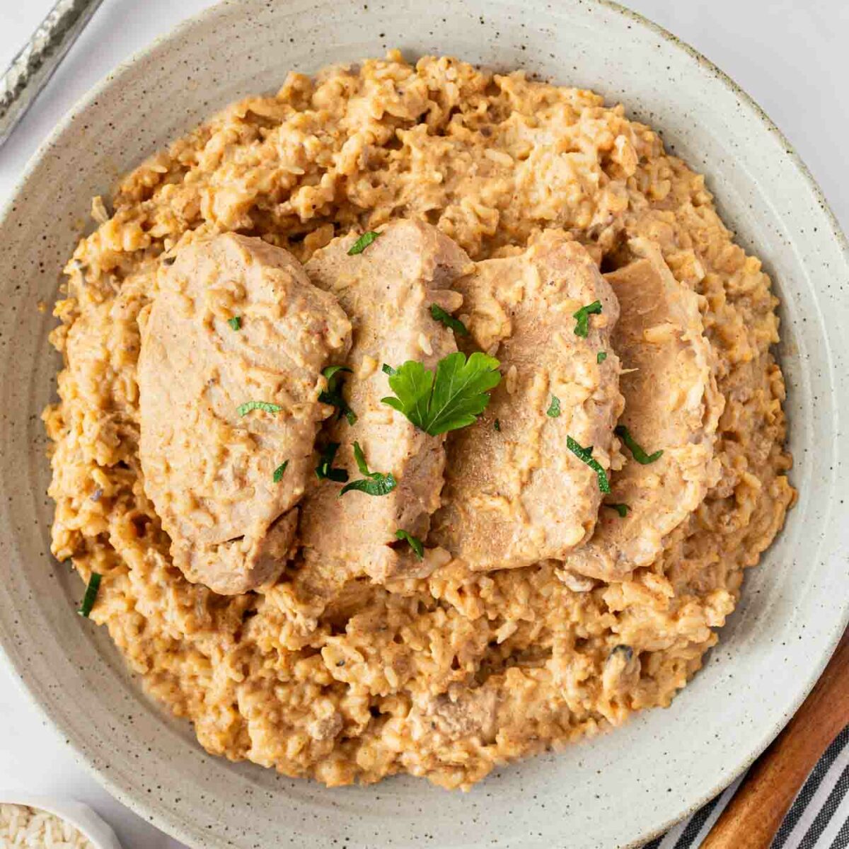 four pork chops nestled on top of creamy rice in a white dish