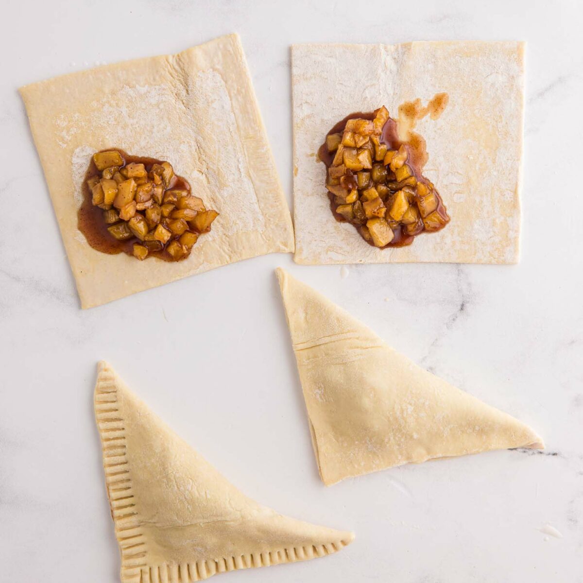 Two square pieces of puff pastry with apple filling are shown, one being folded into a triangle. Another triangle is sealed with fork marks on the edges. The setup is on a white surface.