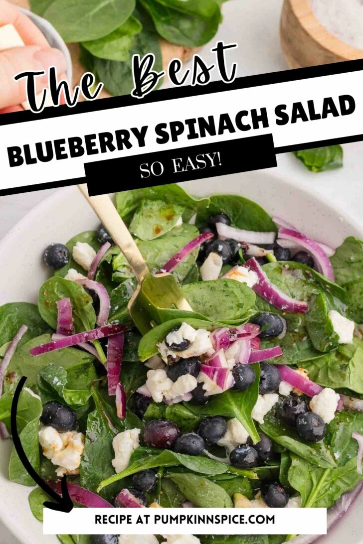 A fresh spinach salad with blueberries, crumbled feta cheese, and sliced red onions in a white bowl. A gold fork rests in the salad. Text overlays read The Best Blueberry Spinach Salad and So Easy! Recipe is from pumpkinnspice.com.