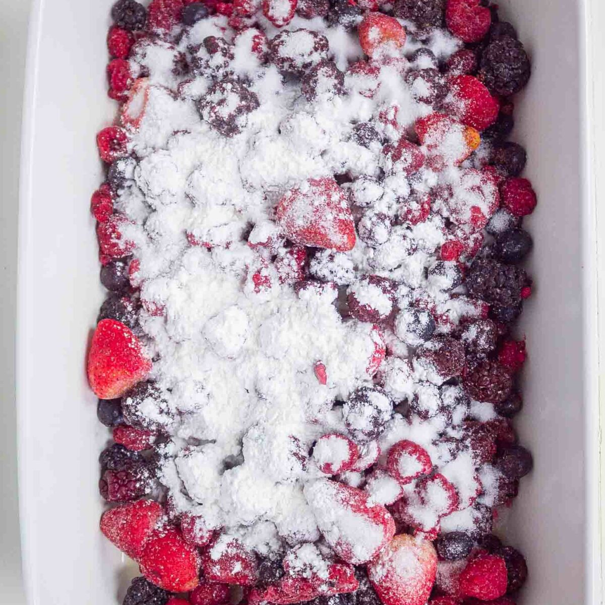 A white baking dish filled with mixed berries and topped with sugar and cornstarch.